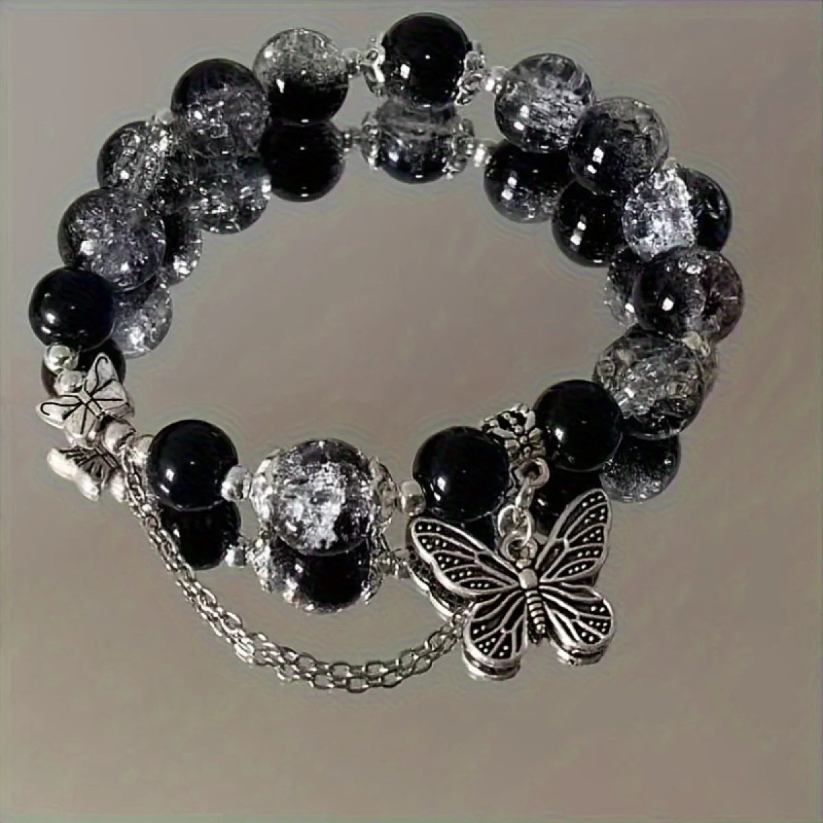 A black beaded bracelet with bohemian style, adorned with silver butterfly pendants and chain details.